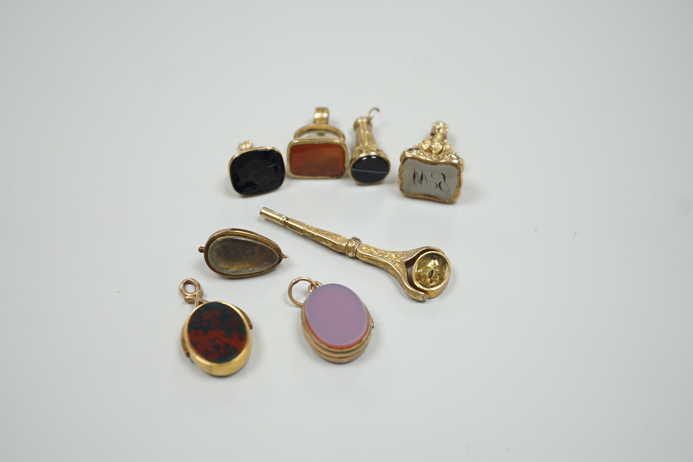 Four assorted 19th century and later yellow metal overlaid and gem set fob seals, a Victorian 15ct gold and sardonyx spinning fob, a sardonyx set locket, damaged pendant and yellow metal and two stone set watch key.